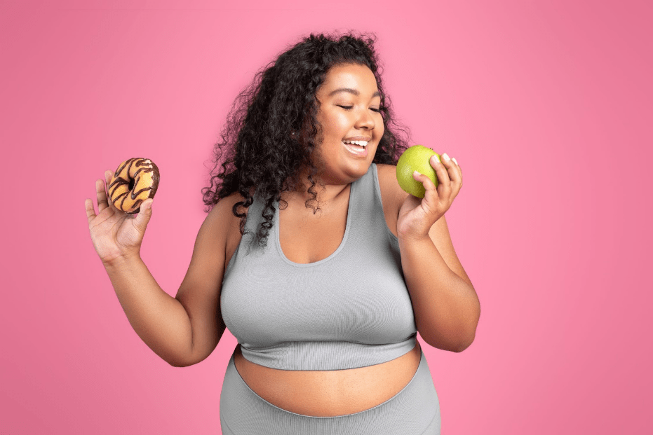 The Science Behind Sustainable Weight Loss - Young black body positive lady in sportswear holding donut and biting apple-min